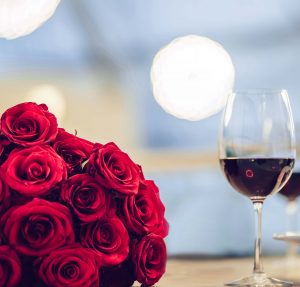 Romantic dinner settings. Two glasses of wine, dishes and bouquet of red roses are on table.